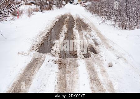 Neve fusa su una superficie asfaltata con acqua profonda e neve sui bordi. Pudddles su una strada innevata all'inizio della primavera. Foto Stock