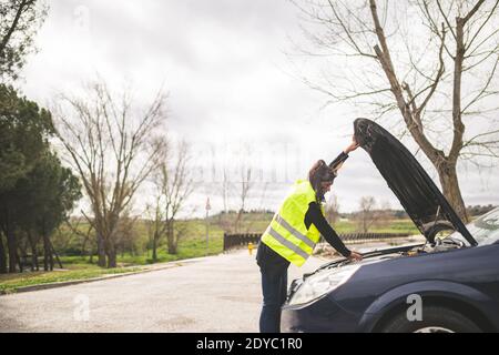 Giovane donna caucasica che guarda il motore dell'automobile, l'automobile rotta giù nel mezzo della strada. Concetto di assistenza stradale e automobilistica. Foto Stock