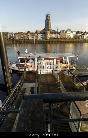 DEVENTER, PAESI BASSI - 16 dicembre 2020: Ponteggio con traghetto in attesa di pendolari per il trasporto attraverso il fiume IJssel con il paesaggio urbano sul retro Foto Stock