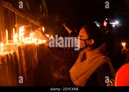 Nuova Delhi, India. 25 Dic 2020. Una ragazza che indossa la maschera illumina le candele fuori della Cattedrale del Sacro cuore in occasione delle celebrazioni natalizie, tra la diffusione della malattia del coronavirus (COVID-19), a Nuova Delhi il 25 dicembre 2020. La più grande chiesa di Delhi, la Cattedrale del Sacro cuore, è stata rinchiusa il Natale per la prima volta a seguito del coronavirus. Credit: David Talukdar/ZUMA Wire/Alamy Live News Foto Stock