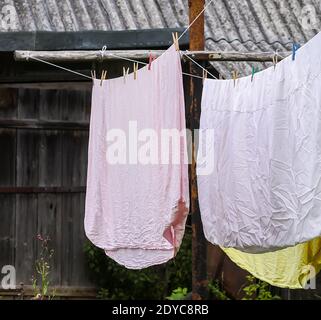 Biancheria da letto appena lavata appesa alla corda all'aperto. Vestiti che asciugano in cortile rurale. Foto Stock