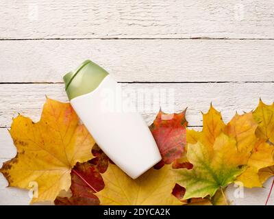 Foglie gialle, shampoo naturale organico su sfondo bianco di legno. Bellezza mockup Foto Stock