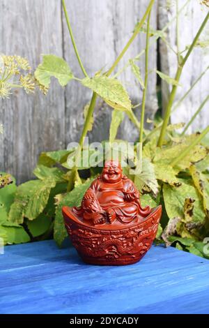 Statuina di buddha in ceramica su tavole di legno blu invecchiate nel parco estivo con fiori. Foto Stock