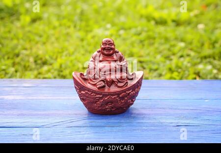 Statuina di buddha in ceramica su tavole di legno blu invecchiate nel parco estivo su sfondo verde erba . Foto Stock