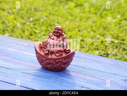 Statuina di buddha in ceramica su tavole di legno blu invecchiate nel parco estivo su sfondo verde erba . Foto Stock