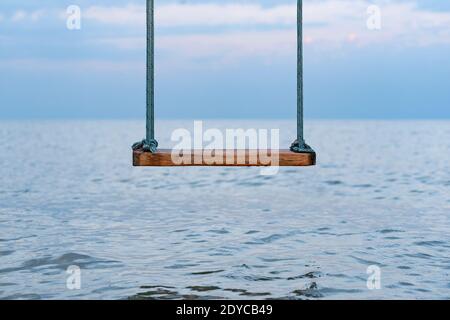 Altalena di legno con corde che si affacciano sul mare. Altalena sulla riva del mare. Foto Stock