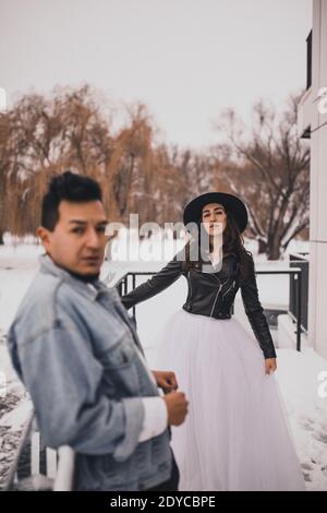 Uomo messicano ispanico in denim oversize giacca e donna in giacca biker in pelle di cappello che bacia il hugging ridendo matrimonio sposa walking.groom coppia d'amore Foto Stock