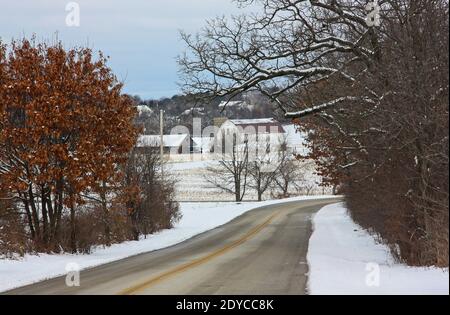 Una strada rurale che passa attraverso un paesaggio innevato e fienile nel Wisconsin rurale. Foto Stock