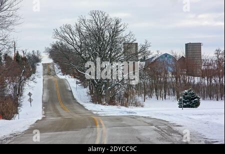 Una strada collinare che passa attraverso un paesaggio innevato e fienile in Wisconsin rurale. Foto Stock