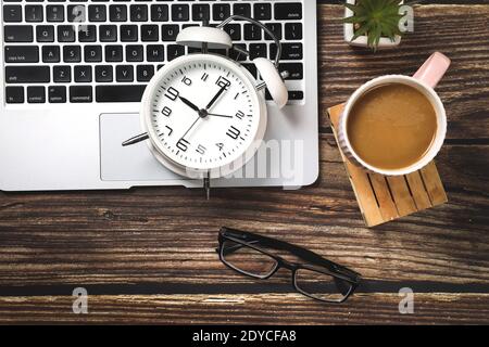 Vista dall'alto del tavolo da lavoro da ufficio con computer portatile, rifornimenti, caffè e sveglia. Concetto di mattina o di scadenza. Foto Stock