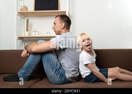 Papà e figlio sono seduti di fronte l'uno all'altro. Padre serio e figlio giocoso Foto Stock