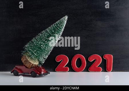 L'auto giocattolo porta il piccolo albero di Natale sullo sfondo dell'iscrizione 2021. Il nuovo anno è in arrivo. Foto Stock