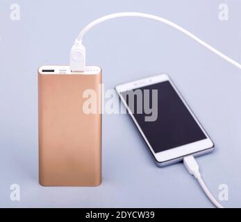 Ricarica dello smartphone con power bank e telefono su sfondo grigio. Foto Stock