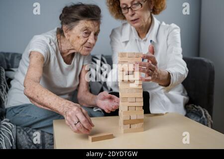 Jenga gioco. Il tema è la demenza, l'invecchiamento e i giochi per gli anziani. Caucasica anziana costruisce torre di blocchi di legno con l'aiuto di un medico come parte Foto Stock