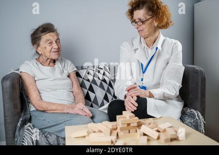 La terapia della demenza in modo giocoso, addestrando le dita e le abilità motorie fini, costruisce i blocchi di legno nella torre, giocando Jenga. Donna anziana di 90 anni e. Foto Stock