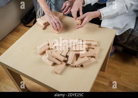 La terapia della demenza in modo giocoso, addestrando le dita e le abilità motorie fini, costruisce i blocchi di legno nella torre, giocando Jenga. Donna anziana di 90 anni e. Foto Stock