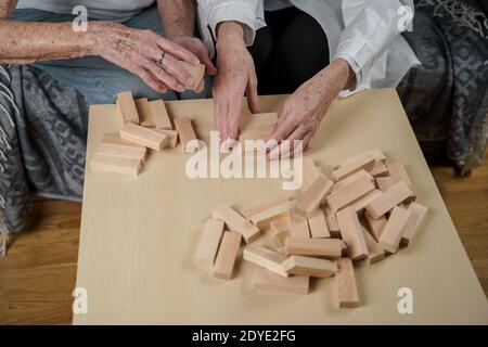 Donna anziana che gioca Jenga, costruisci la torre dei blocchi. Medico anziano in camice di laboratorio bianco, supportando il paziente anziano, sviluppando la logica, le abilità motorie fini Foto Stock