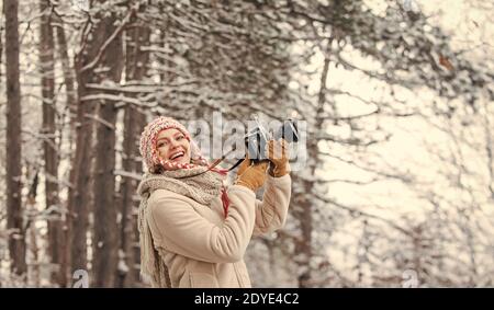 donna in possesso di fotocamera. foto nella foresta d'inverno. Fotografo fotografa sulla neve giorno invernale. Donna felice abiti caldi moda. Vacanza invernale viaggio. Viaggiatore elegante hipster. Foto Stock