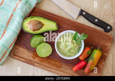 Mezzo avocado, alcuni peperoni caldi e un lime su una tavola di legno e ciotola con la salsa di guacamole Foto Stock