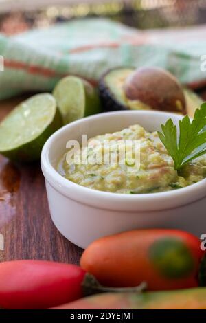 Mezzo avocado, alcuni peperoni caldi e un lime su una tavola di legno e ciotola con la salsa di guacamole. Foto Stock