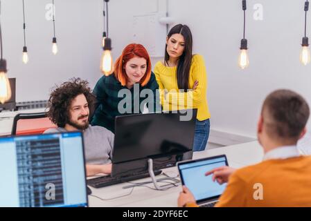 Due giovani donne d'affari accanto a un collega maschile mentre spiega le nuove attività online su un computer in un ambiente di ufficio confortevole. Foto Stock