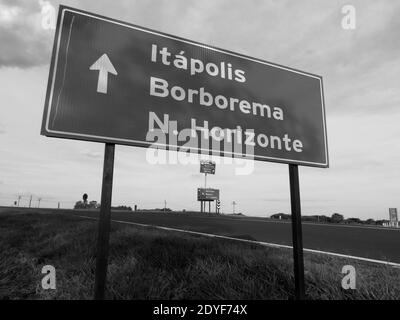 Piastra metallica che dà la direzione di tre città (nomi visualizzati in portoghese) con una grande freccia bianca Foto Stock