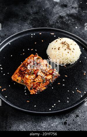 Filetto di salmone alla griglia di Teriyaki giapponese smaltato in deliziosa salsa con un contorno di riso. Sfondo nero. Vista dall'alto Foto Stock