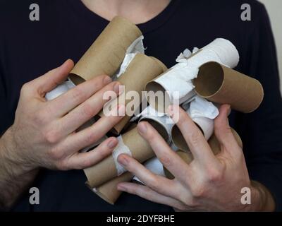 Un paio di mani maschili tengono molti rotoli di carta igienica di cartone vuota TP da vicino. Foto Stock