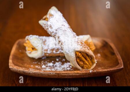 Pumpchiln cannolli ricoperti di zucchero in polvere su un piatto di legno, primo piano Foto Stock