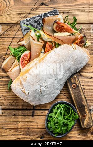 Sandwich con ciabatta, prosciutto, fichi, rucola e prosciutto su una scissione. Sfondo di legno. Vista dall'alto Foto Stock
