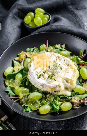 brie al forno, Camembert con uva, bietole e rucola. Sfondo nero. Vista dall'alto Foto Stock