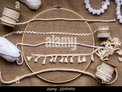 Molti tipi diversi di nastri, rivestimenti e corde in tonalità naturali su un tessuto di tela in un cerchio da ricamo di bambù Foto Stock
