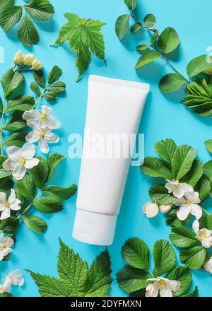 Tubo di plastica bianco per marcare a caldo e fiori bianchi piccoli con verdi su un fondo turchese saturo. SPA prodotto cosmetico. Fiore piatto posa e moc Foto Stock