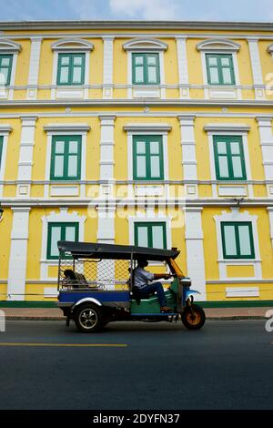 Un tuk tuk nella strada di bangkok con un vista architettonica con finestra verde su un edificio asiatico Foto Stock