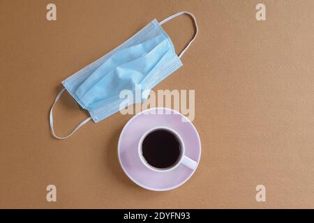 vista dall'alto di una tazza da caffè e rimozione della maschera chirurgica medica su un tavolo marrone. Concetto di protezione. Concetto minimo di salute e allergie. Spazio fo Foto Stock