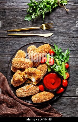 Suppli al telefono fast food italiano - crocchette di riso fritto farcite con mozzarella servite su un piatto nero con gambi di sedano, pomodori e ketchup Foto Stock