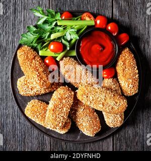 Suppli al telefono fast food italiano - crocchette di riso fritto farcite con mozzarella servite su un piatto nero con gambi di sedano, pomodori e ketchup Foto Stock