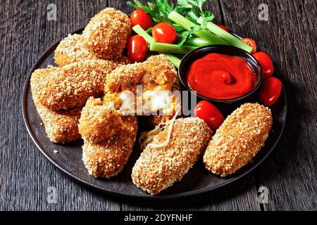 Suppli al telefono fast food italiano - crocchette di riso fritto farcite con mozzarella servite su un piatto nero con gambi di sedano, pomodori e ketchup Foto Stock