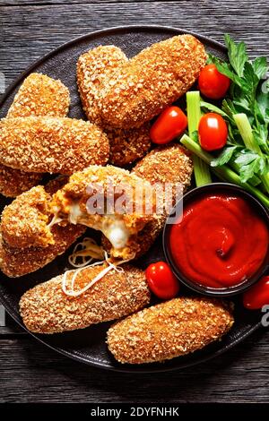 Suppli al telefono fast food italiano - crocchette di riso fritto farcite con mozzarella servite su un piatto nero con gambi di sedano, pomodori e ketchup Foto Stock