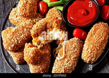 Suppli al telefono fast food italiano - crocchette di riso fritto farcite con mozzarella servite su un piatto nero con gambi di sedano, pomodori e ketchup Foto Stock