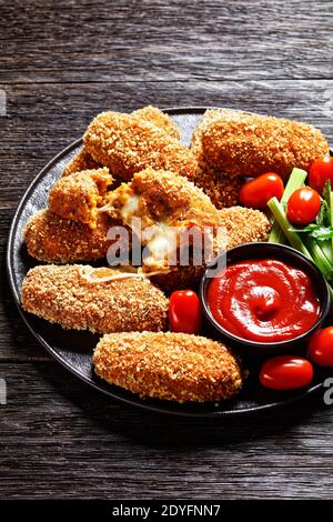 Suppli al telefono fast food italiano - crocchette di riso fritto farcite con mozzarella servite su un piatto nero con gambi di sedano, pomodori e ketchup Foto Stock