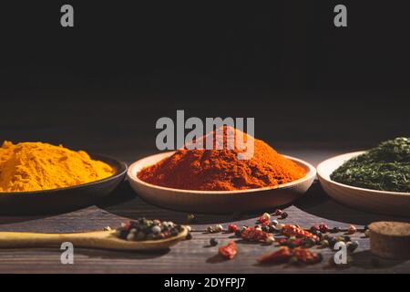 Varie erbe e spezie colorate su tavolo di legno. Sfondo scuro con spazio per la copia. Cucina ingredienti e condimenti concetto. Foto Stock