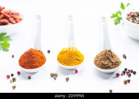 Tre cucchiai bianchi con paprika, curcuma e cumino su fondo bianco. Cucina ingredienti e condimenti concetto. Foto Stock