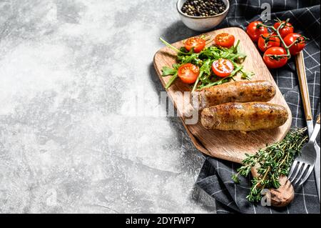 Grigliate di maiale salsicce con contorno di insalata di pomodoro e rucola. Sfondo grigio. Vista dall'alto. Spazio di copia Foto Stock