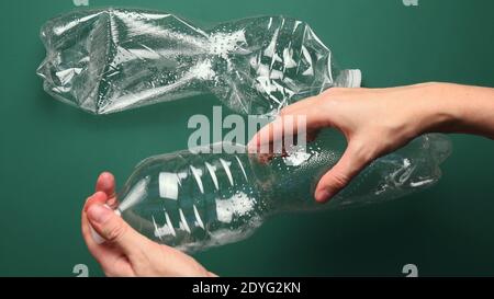 Le mani femmina POV trattengono e svitano il tappo dal flacone di plastica PET trasparente per il riciclaggio. Svuotare i flaconi su sfondo verde. Preparazione prima vista punto Foto Stock