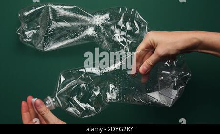 Le mani femmina POV trattengono e svitano il tappo dal flacone di plastica PET trasparente per il riciclaggio. Svuotare i flaconi su sfondo verde. Preparazione prima vista punto Foto Stock