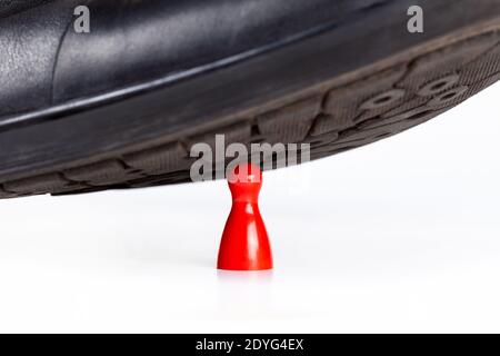 Scarpa nera elegante che batte e schiacciando un piccolo pezzo di pegno rosso sotto il tallone, closeup. Grande contro piccolo, pericolo, tensione e ansia astratta Foto Stock