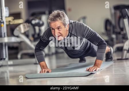 I maschi anziani rimangono in forma facendo pushup su un tappetino all'interno del centro fitness. Foto Stock