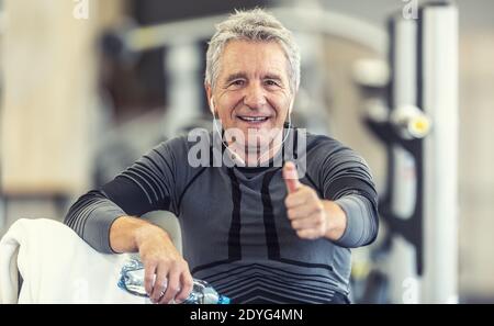 L'uomo con i capelli grigi tiene i pollici in su dopo un workout come mantenersi in forma indipendentemente dall'età. Foto Stock