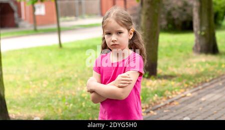 Un solo offeso bambino, triste ansioso arrabbiato lone ragazza in piedi leggermente sconvolto, capretto con le braccia incrociate, closeup, ritratto, all'aperto, spazio di copia Foto Stock